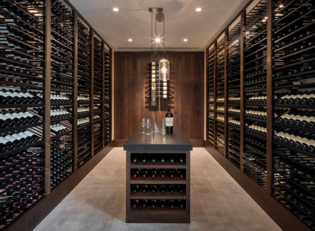 Private bottle cellar with wood racks and central island with wine and glasses.