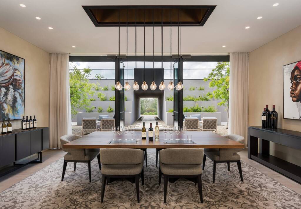 A spacious hospitality room with a large central table, artwork, and dramatic pendant lights.