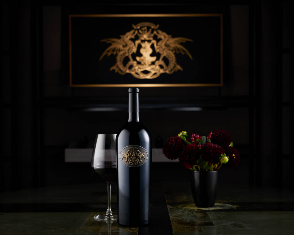 Draco Dormiere bottle and glass with gold logo artwork in background and arrangement of flowers.