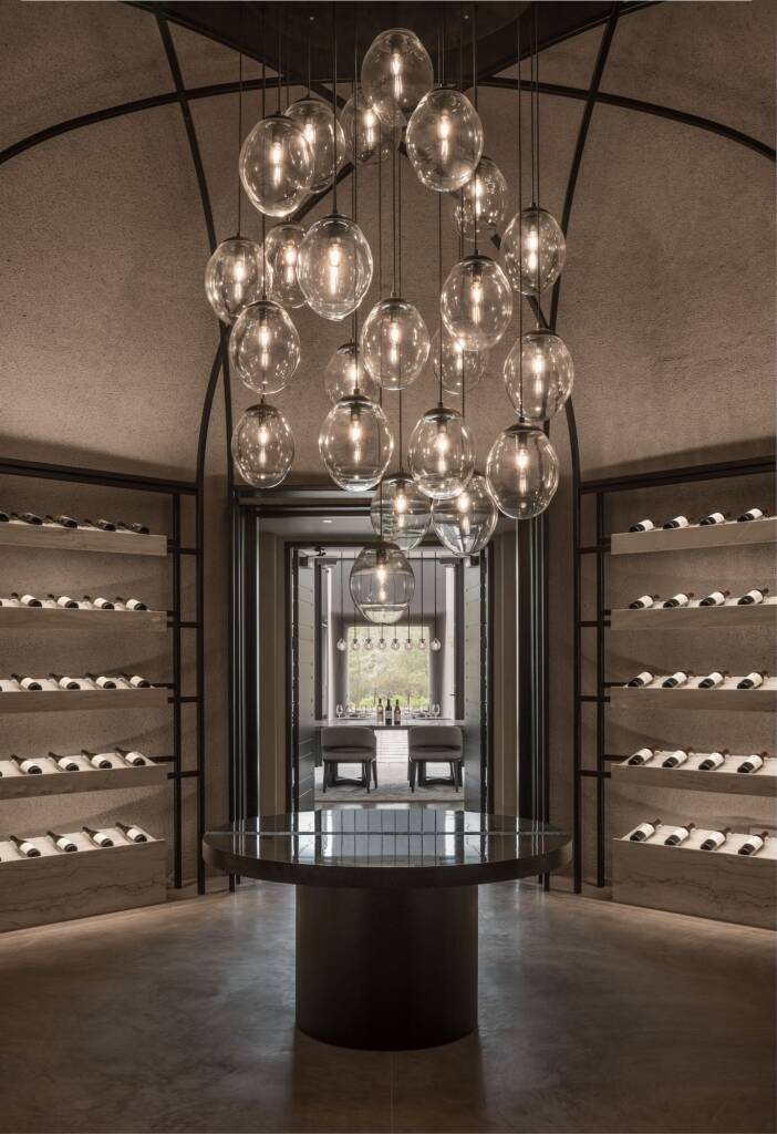 Dramatic round wine room with under-lit wines displayed on the walls and modern glass chandelier.